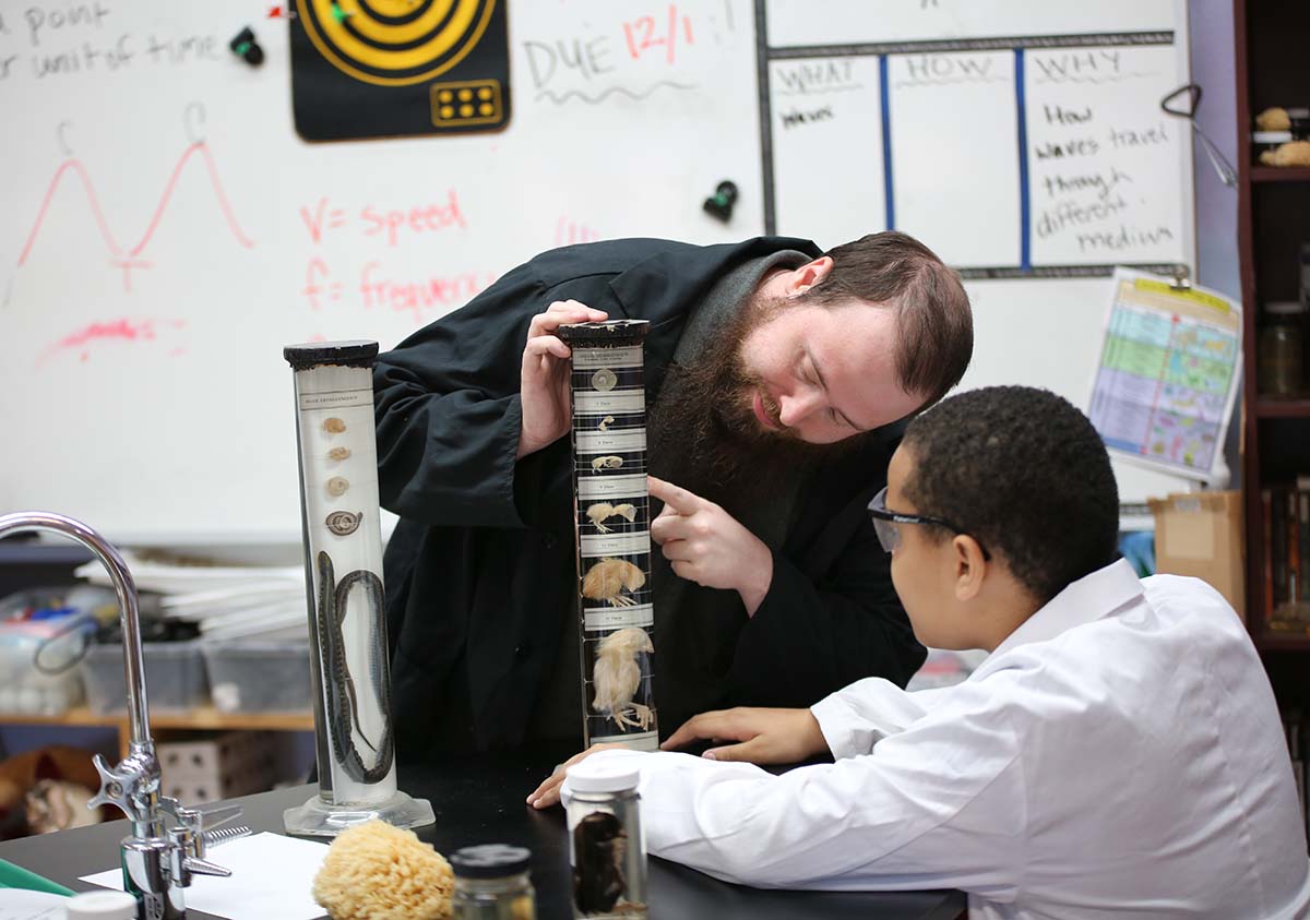 HSA Teacher smiles while kneeling beside a young student in a classroom setting.